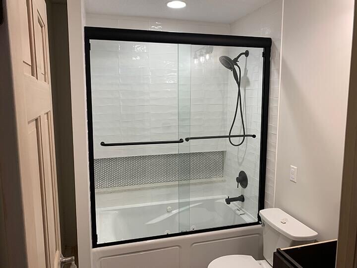 Black-framed sliding glass tub doors in a white subway-tile bath