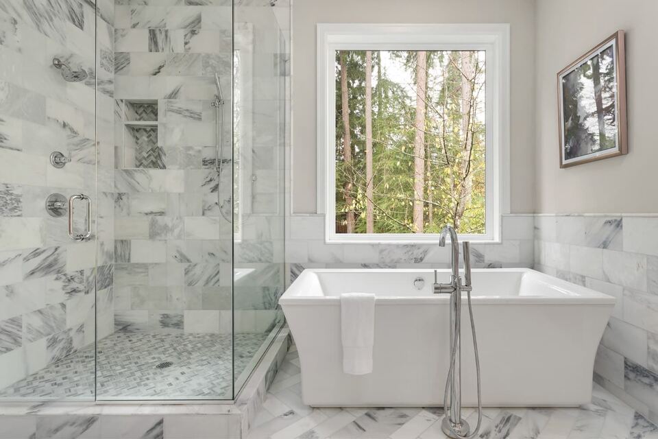 Frameless glass shower next to a freestanding soaking tub under a window