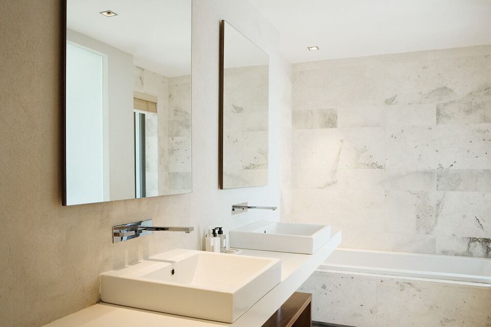 Frameless vanity mirrors above two vessel sinks in a marble bathroom